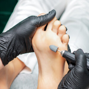 Pedicure master is polishing foot of woman with special machine tool, close up.